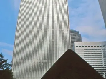 Cloud Fortress, a dark triangular sculpture on a paved plaza with a skyscraper rising behind it.