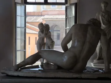 Cupid and Psyche marble sculpture seen in a window with rooftops beyond, partially obscured by a reclining marble figure in the foreground.