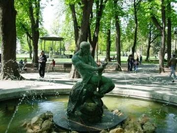 Fisherman Fountain bronze statue of a man wrestling a serpentine creature in a park with trees and paths.