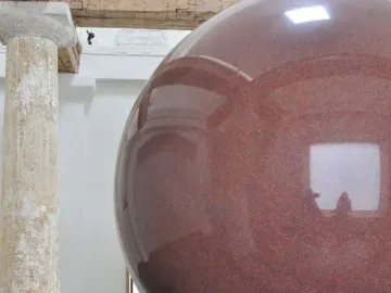 Large Red Sphere sculpture on a two-tiered circular pedestal in a bright interior space.