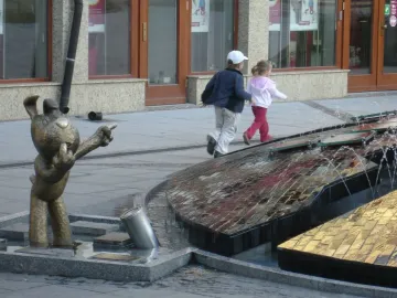 Reksio Monument beside a modern fountain, with a bronze dog figure standing in a shallow pool.