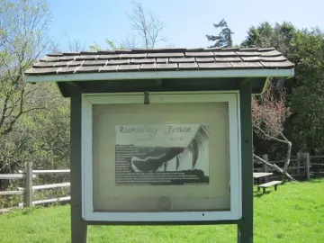 Informational kiosk for Running Fence stands on a grassy lawn near a split-rail fence.