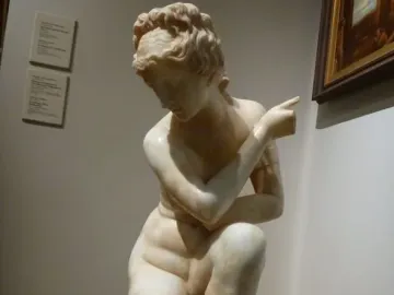 Crouching Venus marble statue of a crouching nude female figure displayed on a pedestal in a gallery