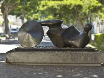 The Goslar Warrior bronze sculpture in an outdoor setting, shown as a dark abstract recumbent figure with a round disc form at one end.