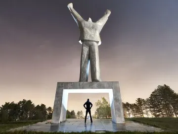 Monument to Stjepan Filipović, a tall abstract concrete statue with raised arms above a lit pedestal arch and silhouetted figure.