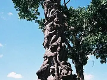 Pillar of Shame sculpture with writhing human figures on a tall dark pillar and plaque at the base.