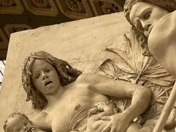 Close-up of The Nubians sculpture showing a distressed woman holding two infants among foliage, with a long stick crossing the lower right.