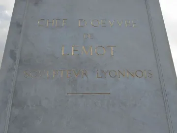Close-up of a carved stone inscription panel on the Louis XIV equestrian statue, with gold-lettered text and a decorative line.