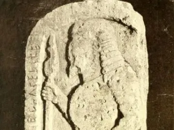 Stele of Avile Tite showing a carved warrior in profile with a spear and round shield on a weathered stone slab.