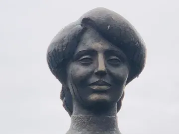 Bronze statue of Zabel Yessayan holding a book against her chest and looking upward.