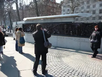 The Battle of Britain Monument with a silver sculpture above dark relief panels and carved stone text, with people standing nearby.