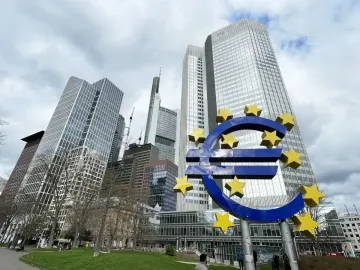 Blue euro sculpture with yellow stars in front of Frankfurt skyscrapers and a cloudy sky.