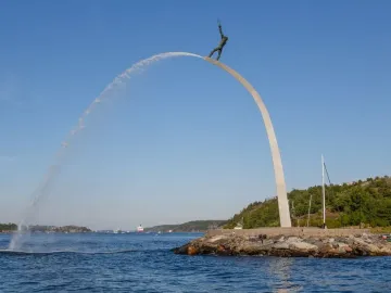 God our Father on the Rainbow sculpture with water arcing into the bay beside a rocky shoreline