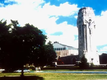 The National Shrine of the Little Flower with a tall stone tower and Christ figure beside a rounded building, framed by trees and a grassy foreground.