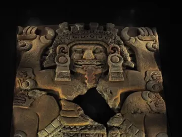 Tlaltecuhtli Monolith with a fanged mouth, elaborate headdress, and clawed limbs in reddish-brown stone.