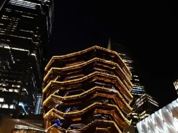The Vessel glowing with golden lights at night, with people gathered around its base.