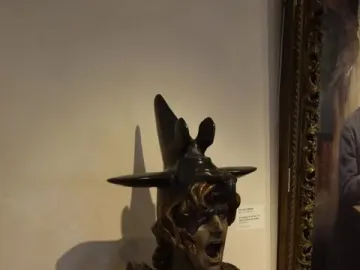 Bellona bust with a winged helmet and open mouth displayed on a white pedestal.