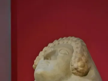 Stone head of the Lady of Cádiz sculpture with curled hair and a serene face against a red background.