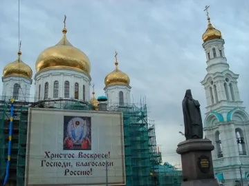 Monument to Dimitry of Rostov in front of a church with golden domes and a bell tower under restoration netting.