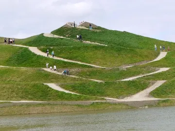 Northumberlandia’s grassy sculpted hill with winding paths and people walking along the slopes beside water.