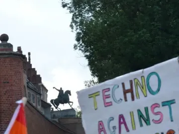 Tadeusz Kościuszko Monument seen as a dark silhouette atop a brick bastion above a colorful crowd and protest banners.