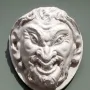 White circular relief sculpture of the Head of a Faun with a grinning face, pointed ears, and curly beard and hair.