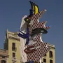 The Face of Barcelona sculpture with red dots, yellow-and-black stripes, and blue mosaic tiling against a blue sky.