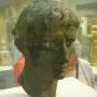 Meroë Head bronze sculpture with short curly hair and prominent eyes on a pedestal