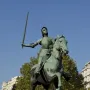 Joan of Arc equestrian statue in medieval armor holding a raised sword on a stone pedestal in Paris.