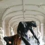 The Shade sculpture by Rodin in a museum hall, with a person posing beside it in a similar bent-forward stance.