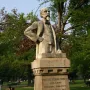Monument to Ernesto Teodoro Moneta on a tall stone pedestal in a park, with trees and people on the lawn behind it.
