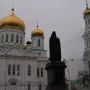 Monument to Dimitry of Rostov in front of a white Orthodox cathedral with golden domes and a bell tower.
