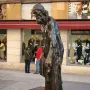 Eustache de Saint Pierre bronze sculpture of a bearded man in long robes standing on a stone base beside storefront windows