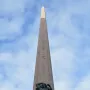 The Obelisk of Montevideo rises against a blue sky, with bronze figures at its base.