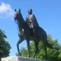 Elizabeth II equestrian statue on a stone pedestal with green foliage and blue sky behind it