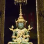 The Emerald Buddha seated on a golden pedestal beneath an ornate canopy with gilded columns and jeweled decorations.