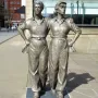 Women of Steel bronze sculpture of two women standing arm in arm in work clothes.