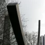 Bernar Venet’s Arc de 124,5° sculpture rising over a grassy area with bare trees and city buildings in the background.