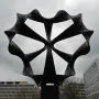 Continuum sculpture with dark, looping metal forms radiating from a central point against a cloudy sky.