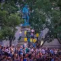 Albert Pike Memorial statue surrounded by a crowd holding candles and protest signs.