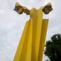Ángel Custodio, a tall yellow abstract sculpture with curved wing-like shapes in a park.