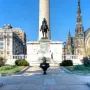 Lafayette Monument with a dark equestrian statue on a stone pedestal, a tall cylindrical monument behind it, and churches and buildings around the plaza.