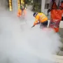 Workers clean the Pankhurst Memorial pavement with a high-pressure washer beside a wrapped vertical structure.