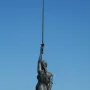 Verity sculpture seen from behind, holding a raised sword and scales against a blue sky.