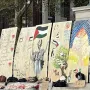 Lower portion of Alma Mater is partially visible behind protest signs and a metal barrier, with the base and part of the name visible.