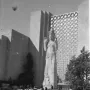 Pacifica statue stands before a geometric exhibition building with crowds gathered around the base.