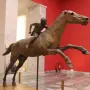 Jockey of Artemision bronze sculpture showing a young rider leaning forward on a horse in motion inside a museum.