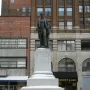 Stevens T. Mason Monument on a snowy stone pedestal beside downtown buildings.