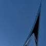 The Life Electric sculpture in Como, a tall reflective silver monument against a deep blue twilight sky and waterfront lights.