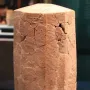 Rassam cylinder covered with dense rows of cuneiform script on a reddish-brown multi-sided prism with visible cracks and missing fragments.